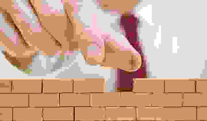 Close up as a man puts the last little brick in a miniature wall