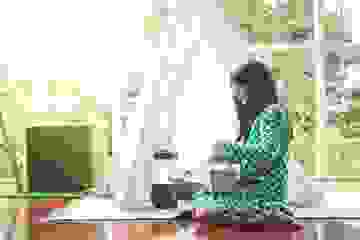 Little girl with long black hair sitting inside wrapping a Christmas present on a bright day