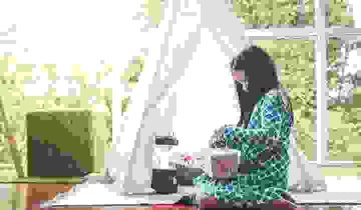 Little girl with long black hair sitting inside wrapping a Christmas present on a bright day
