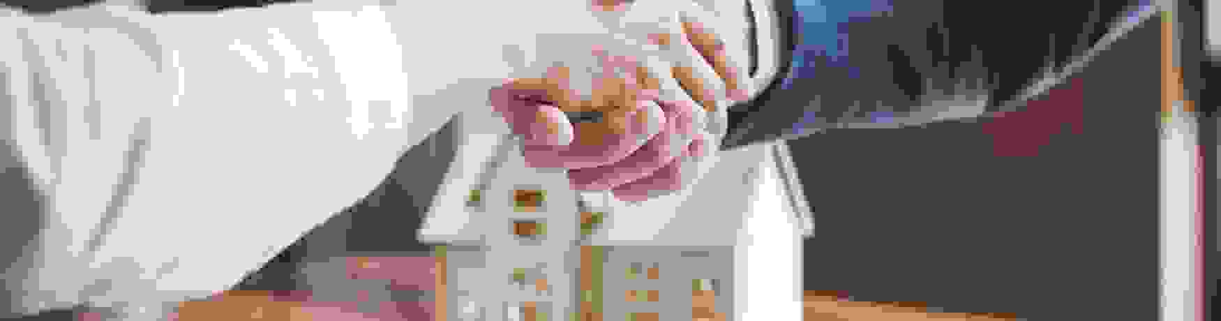 Close up of two people shaking hands over a real estate contract and set of keys with a house model in the background