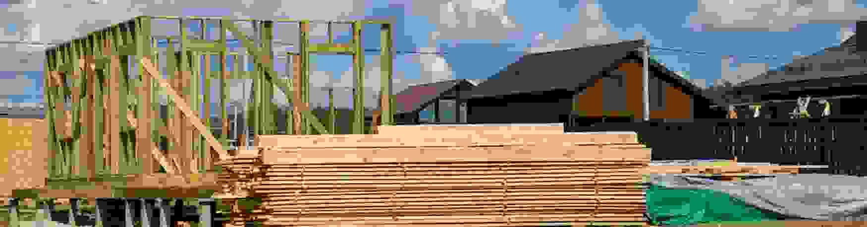 House under construction with timber framing and wood stacked beside the build
