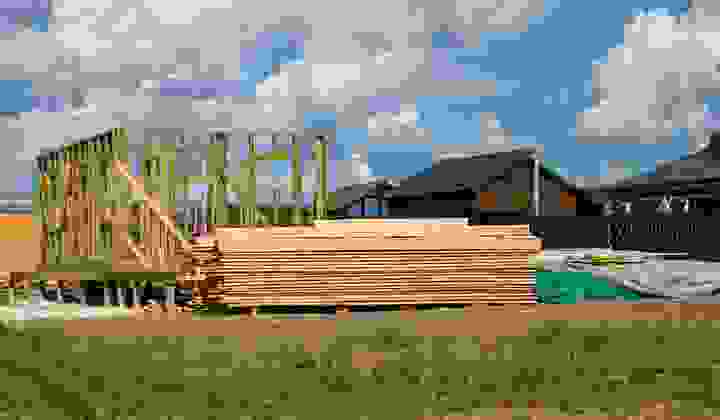 House under construction with timber framing and wood stacked beside the build