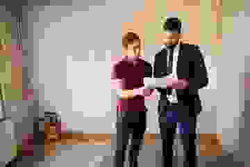 Two men standing in a room that needs renovating, talking over some papers
