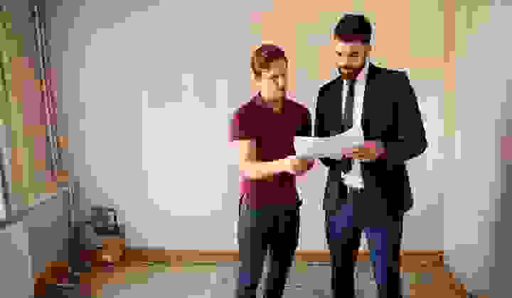 Two men standing in a room that needs renovating, talking over some papers