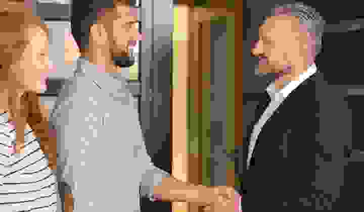 Young couple shaking hands with a property manager outside a house