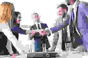 Group of business people in agreement shaking hands over a table with folders and water glasses
