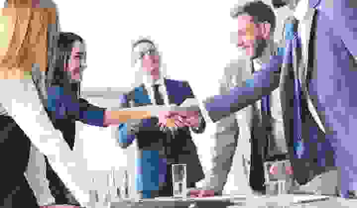 Group of business people in agreement shaking hands over a table with folders and water glasses
