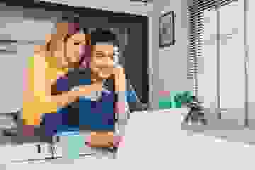 A smiling young couple look at their real estate listings on their laptop at home