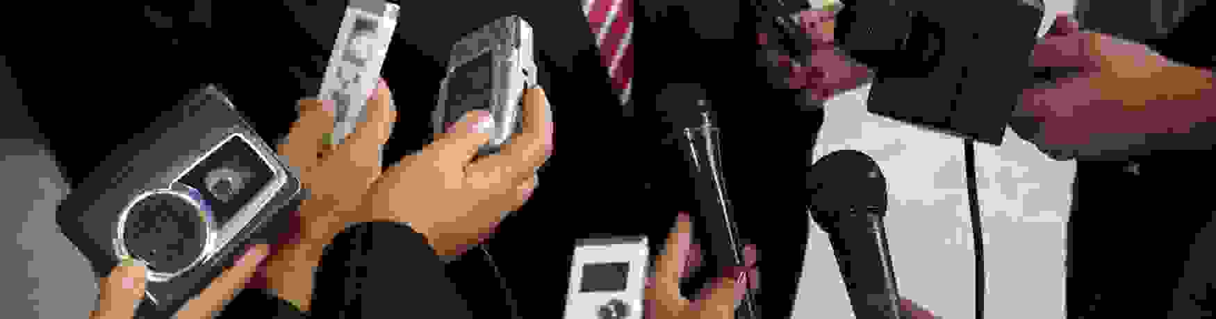 Mid shot of microphones and tape recorders being held in front of a politician for comment