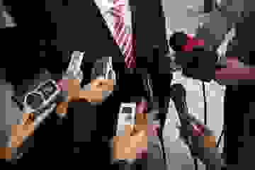 Mid shot of microphones and tape recorders being held in front of a politician for comment