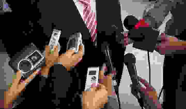 Mid shot of microphones and tape recorders being held in front of a politician for comment